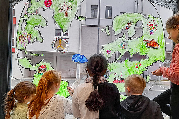 Kinder malen Friedensbild auf Fenster des Caritas-Quartiersbüros