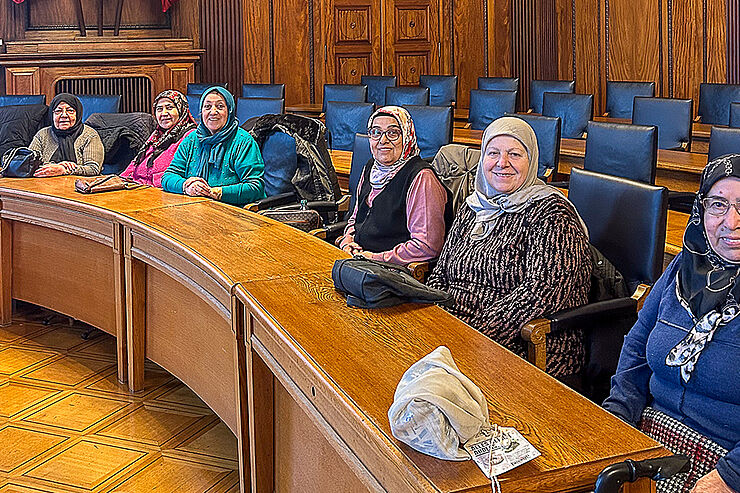 Mehrere Frauen sitzen in einer Reihe auf hohen Holzstühlen.