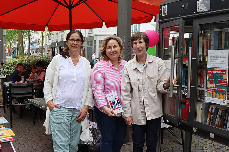 Drei Frauen stehen nebeneinander vor einem Bücherschrank.