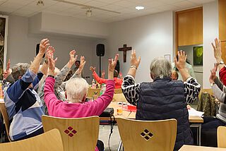 Sitzende Menschen halten ihre Hände nach oben.