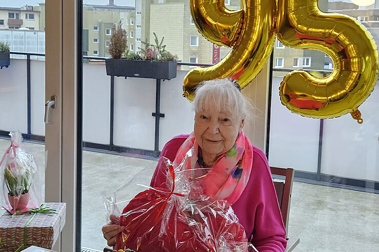 Eine ältere Frau lächelt, im Hintergrund hängt eine große 95.