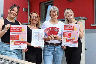 Vier lächelnde Frauen halten Plakate und Bilder in die Kamera.