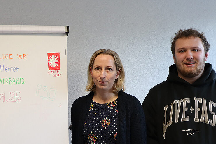 Eine Frau und ein junger Mann stehen neben einer Infowand.