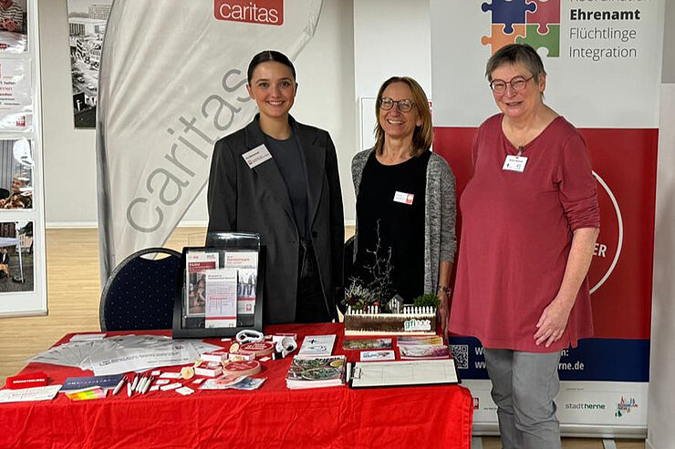 Drei Frauen stehen hinter einem rot-weißen Stand.