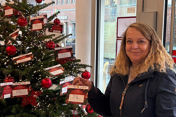Eine Frau nimmt eine bunte Karte vom Weihnachtsbaum.