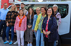 Lachende Gruppe Menschen vor kleinem Reisebus.