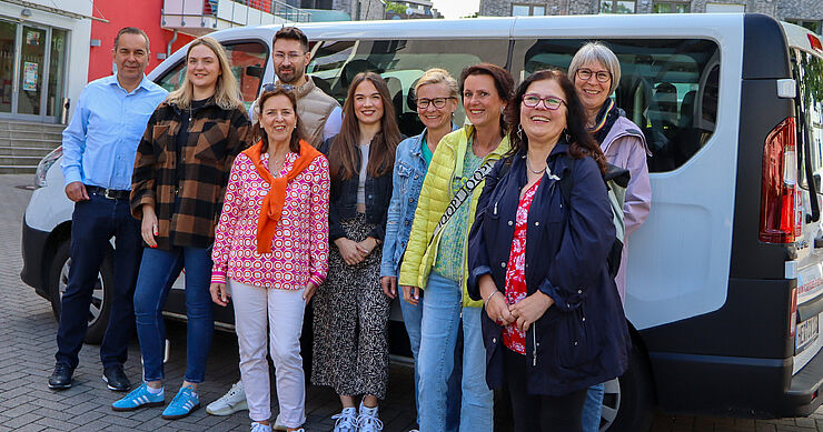 Lachende Gruppe Menschen vor kleinem Reisebus.