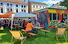Menschen sitzen auf Bänken vor einem bunt bemalten Container.