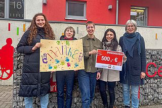 Fünf Frauen stehen zusammen und halten ein buntes Bild mit Aufschrift "Danke" und einen Scheck in den Händen.