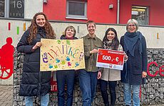 Fünf Frauen stehen zusammen und halten ein buntes Bild mit Aufschrift "Danke" und einen Scheck in den Händen.