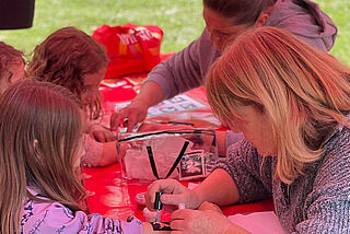 Zwei Frauen machen bei drei Kindern Kindertattoos.