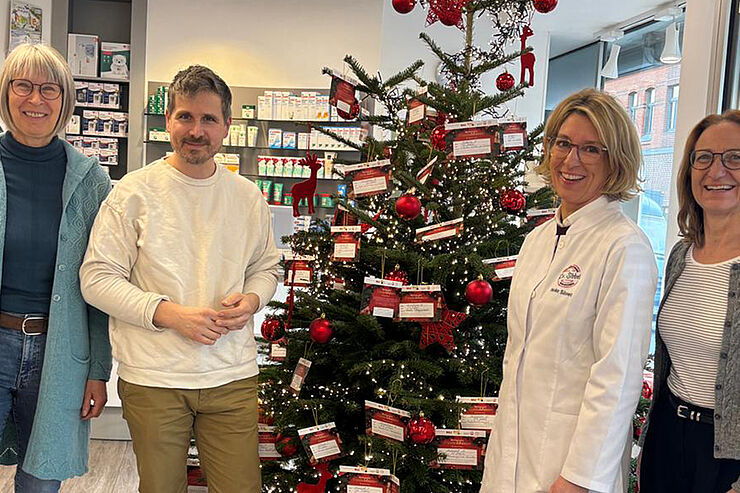 Vier Menschen stehen vor einem Weihnachtsbaum.