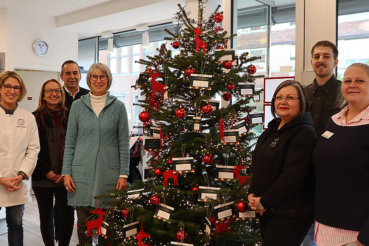 Sieben Personen stehen um einen Weihnachtsbaum herum.