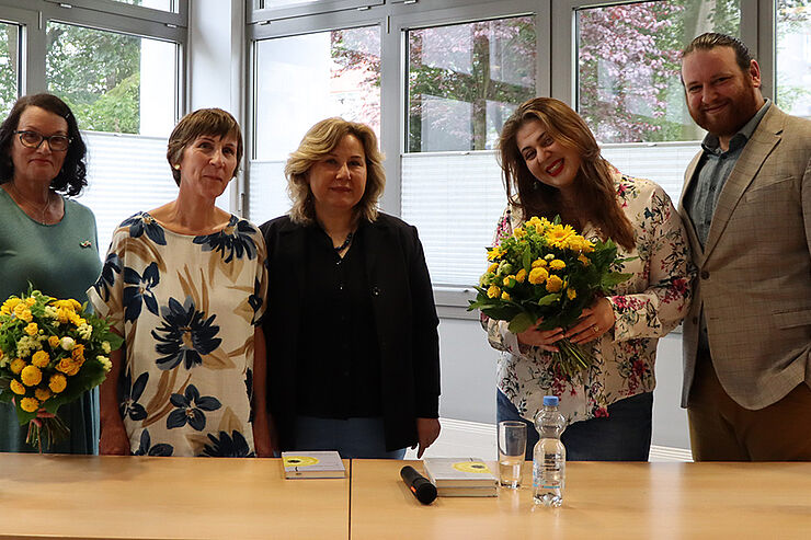 Zwei Frauen mit Blumen, zwei weitere Frauen und ein Mann stehen nebeneinander und lächeln.