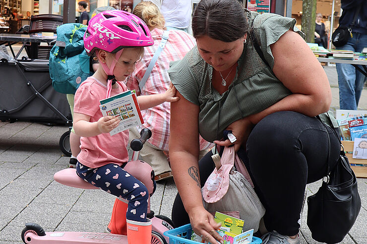 Ein kleines Kind und seine Mutter durchstöbern einen Korb mit Büchern.