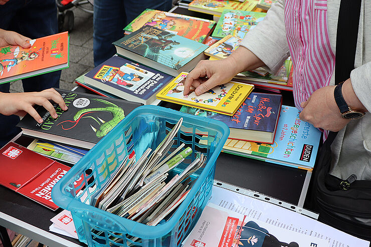 Hände mit Büchern in der Hand und ein Tisch mit vielen Büchern.