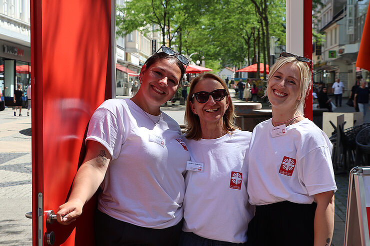 Drei lachende Frauen stehen vor einer offenen roten Tür.