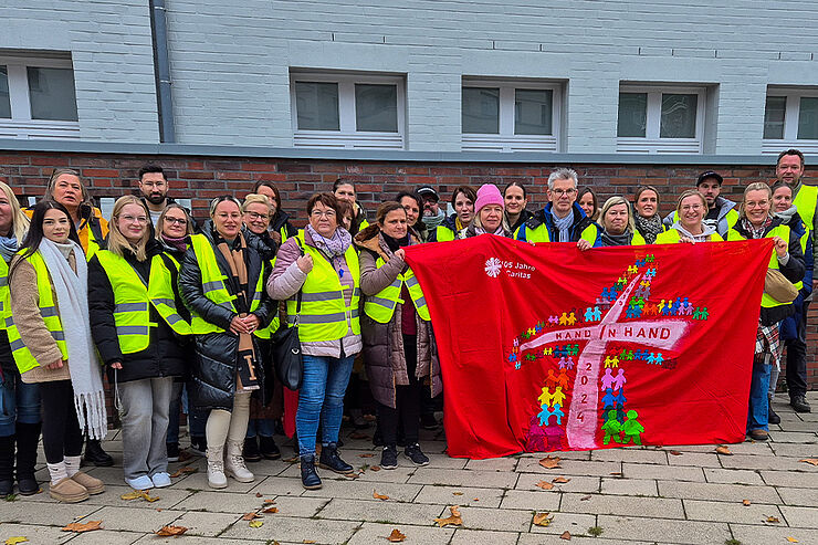 Eine Gruppe Menschen in Warnwesten steht zusammen und hält ein Plakat mit der Aufschrift Hand in Hand.