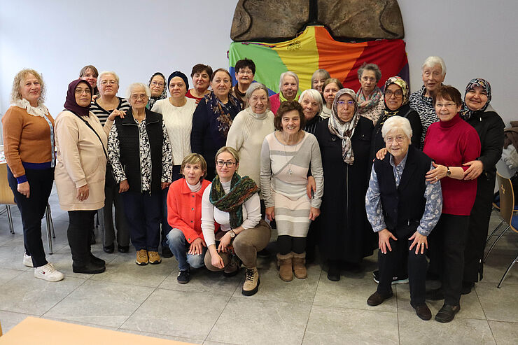 25 Frauen stehen zusammen und lächeln in die Kamera.