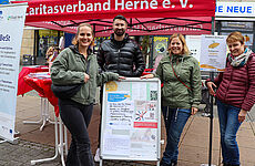 Vier Menschen stehen vor einem Pavillon um einen Aufsteller herum.