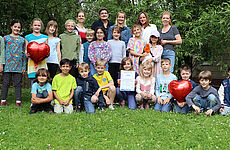 Eine Gruppe von Kindern und Erwachsenen steht und hockt auf einer Wiese.