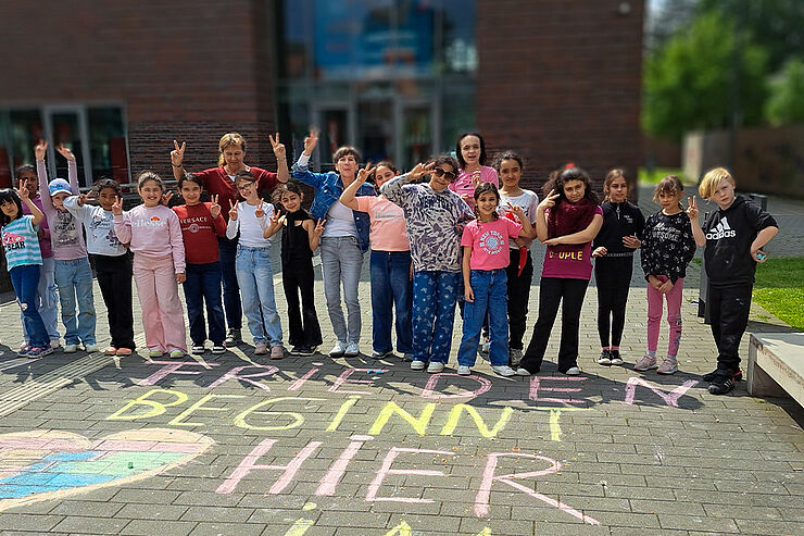 Gruppe aus Erwachsenen und Kindern steht winkend vor dem Museum