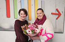 Eine Frau überreicht einer anderen Frau einen Blumenstrauß.