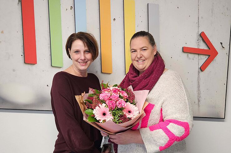 Eine Frau überreicht einer anderen Frau einen Blumenstrauß.