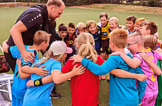 Ein Mann und eine Gruppe Kinder stehen Arm in Arm im Kreis und lachen.
