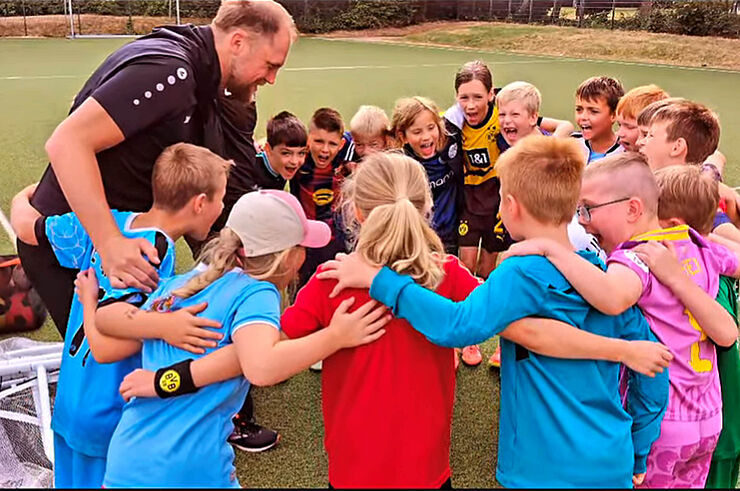 Ein Mann und eine Gruppe Kinder stehen Arm in Arm im Kreis und lachen.