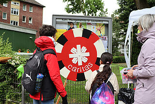 Eine Frau und zwei Kinder stehen vor einem rot-weißen Glücksrad.