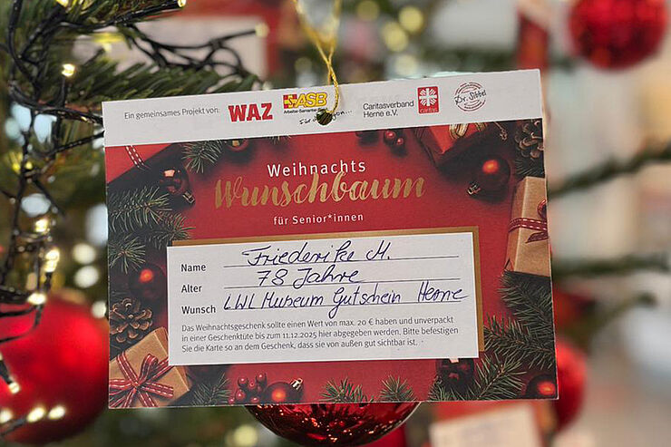 Eine bunte Karte hängt an einem Weihnachtsbaum.