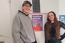 Zwei junge Menschen stehen vor einem Plakat mit der Aufschrift Zusammen geht was.