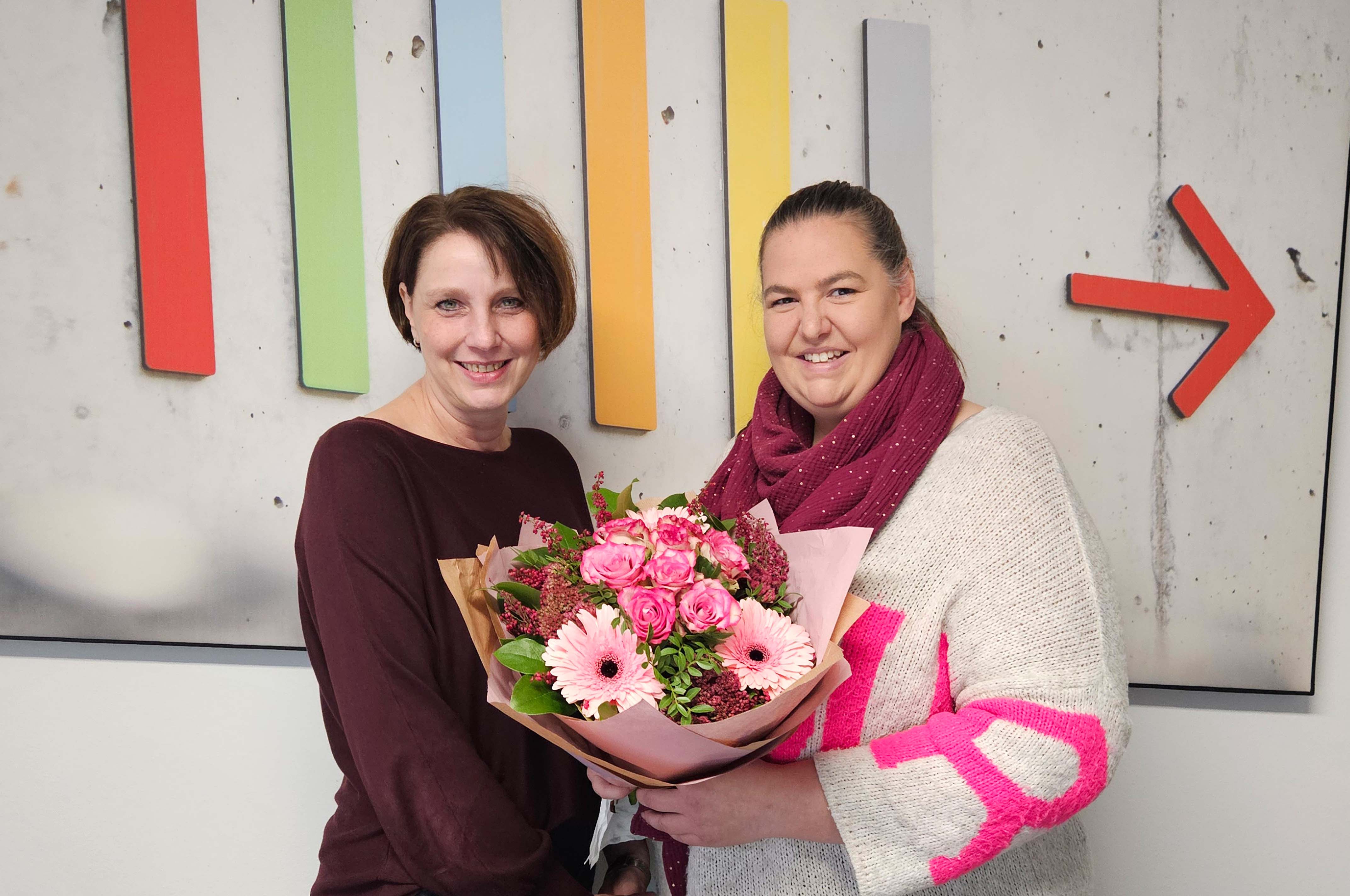 Eine Frau überreicht einer anderen Frau einen Blumenstrauß.